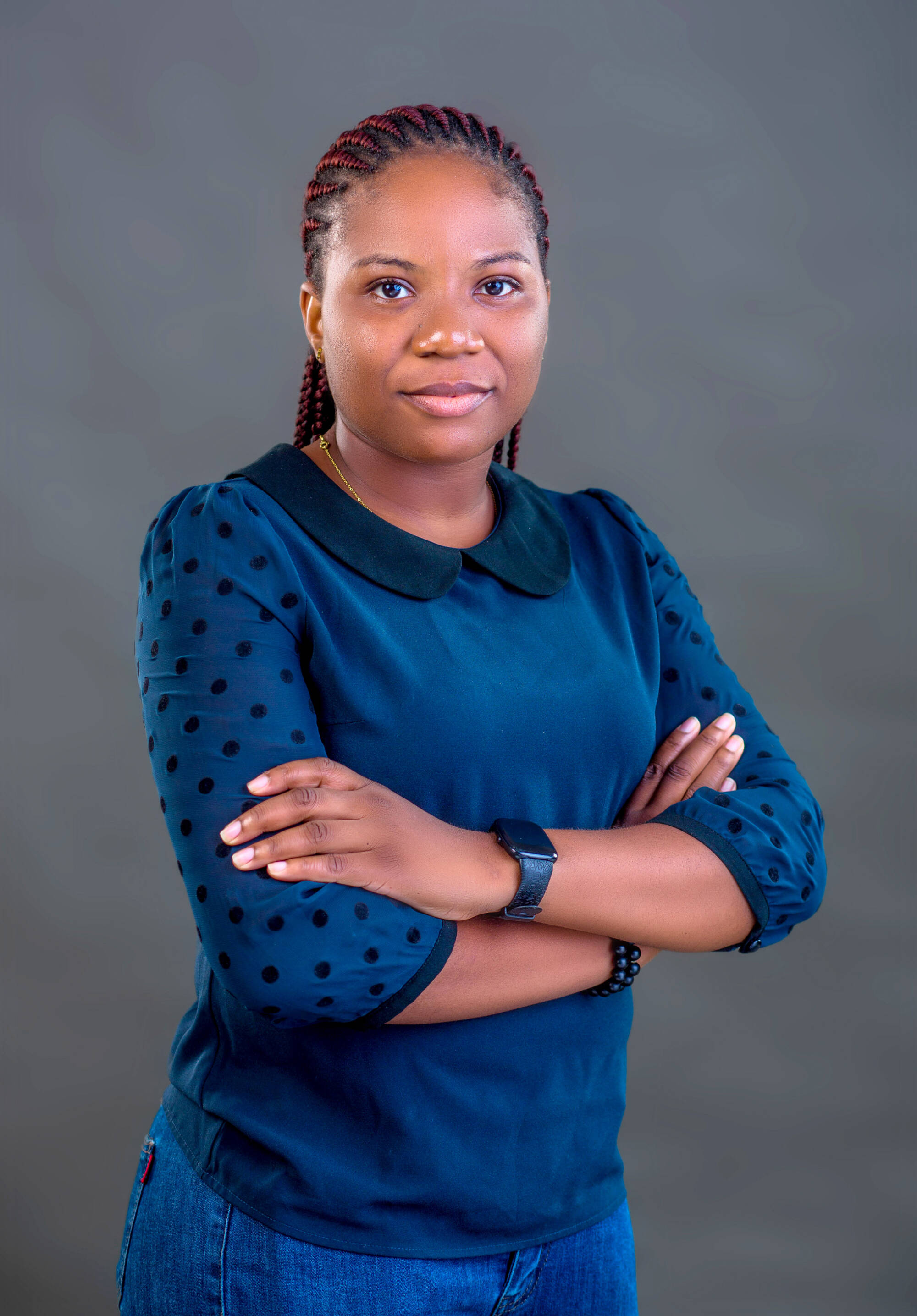 photo of adjunct faculty fiyinfoluwa olajide wearing a royal blue top, against a grey background, with arms crossed and looking at the camera.